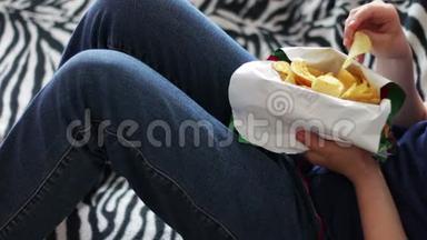 一个十几岁的男孩在家里用手在沙发上吃薯片